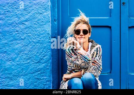 Coloured and trendy lifestyle fashion portrait of beautiful young caucasian middle age woman looking at the camera - blue traditional old home background and door Stock Photo