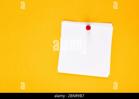 Blank white note paper pinned with a push pin on a yellow notice board Stock Photo