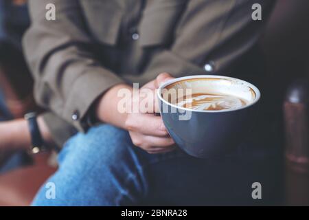 Closeup image of a woman's hand holding and drinking hot latte coffee while sitting in cafe Stock Photo