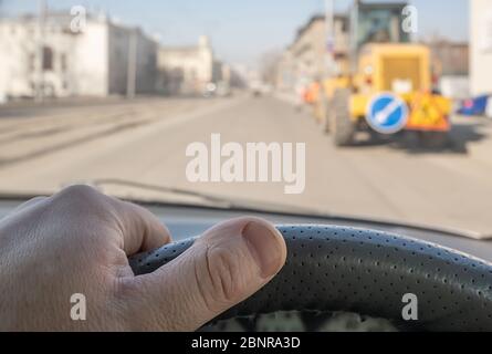 view of the driver hand on the steering wheel of a car passing through the courtyard of the street where the tractor stand Stock Photo