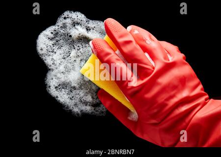 Human hand in a red rubber glove wiping with a sponge on isolated black background. Cleaning, wiping or disinfecting. Stock Photo