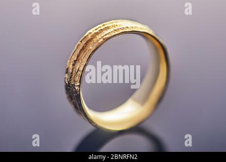 Jewelry making. Yellow gold wedding ring with an unusual texture standing on a gray background. Stock Photo