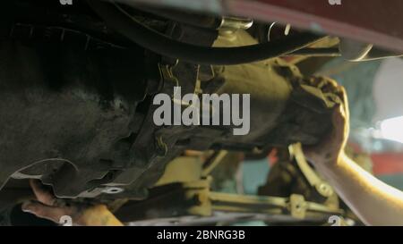 Worker Mechanic unscrewing parts of automobile's bottom under lifted car. Stock Photo