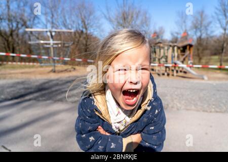 Child is furiously standing in front of a closed playground during the 2020 corona crisis Stock Photo