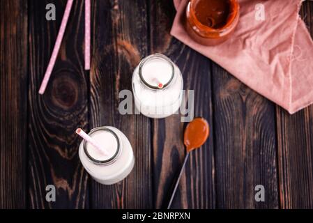 Two bottles of fresh milk with tubes and fresh homemade salted caramel n dark background. Delicious breakfast Stock Photo