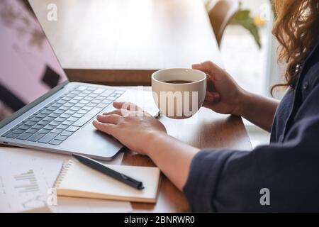 Closeup image of a woman touching on laptop touchpad while drinking coffee and working in office Stock Photo