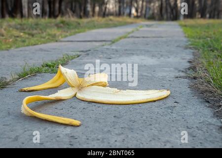 a banana peel lies on a concrete footpath against the backdrop of a city Park Stock Photo