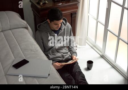 Young man leaves technology to read a book at home. Concept of digital detox, spend time at home. Stock Photo