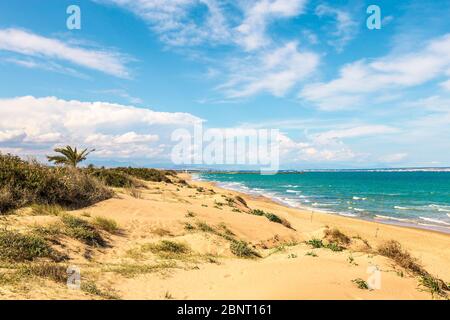 view of sand dunes and beach with green sea and clouded blue sky Stock Photo