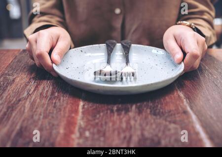 woman sitting and holding a plate with spoon and fork on vintage wooden table in the restaurant Stock Photo
