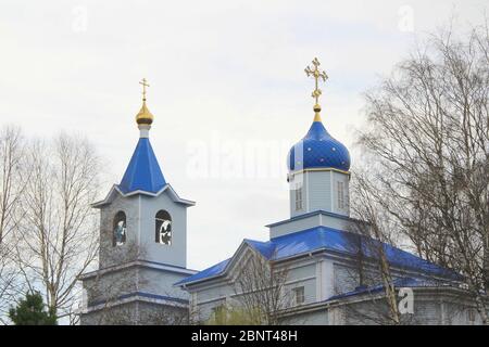 Orthodox Christian church with white walls, blue domes and golden crosses in Russia. A building for religious ceremonies with a bell tower against a cloudy sky in the countryside. Stock Photo