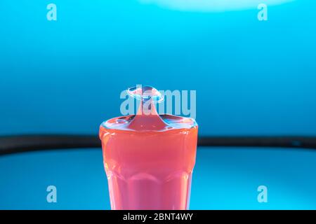 Pink liquid drop falls into glass, hitting liquid surface,forms mushroom shape. Selective focus Stock Photo