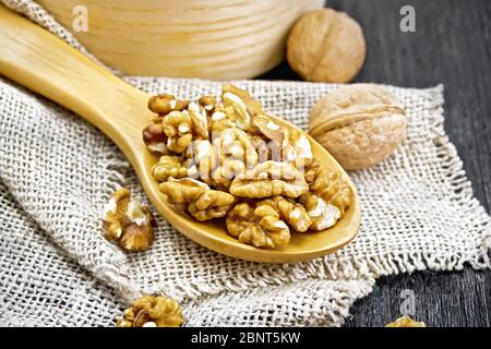 Walnuts peeled in a spoon on burlap, whole nuts in a bowl on background of dark wooden board Stock Photo