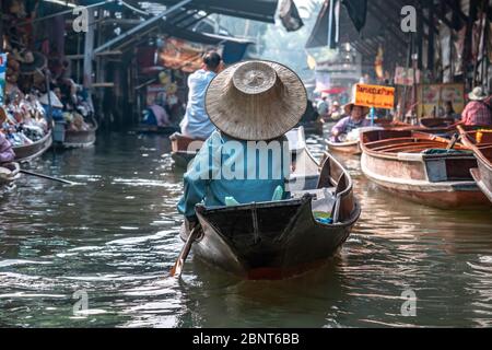 Ratchaburi, Damnoen Saduak / Thailand - February 11, 2020: Name of this place Damnoen Saduak Floating Market. Vendor woman scull the boat with her hat Stock Photo