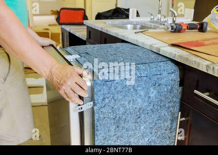 Technician plumber installation of kitchen dishwasher into place Stock Photo