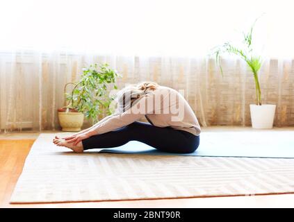 Full body adult female in casual clothes raising arms and stretching body while doing yoga on floor at home Stock Photo