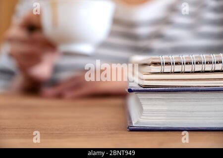 Closeup image of a woman drinking coffee with books and notebooks on wooden table Stock Photo