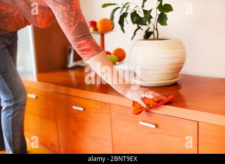 Side view of adult lady in casual clothes removing dust with cloth from shelf while cleaning cozy room at home. Close up Stock Photo