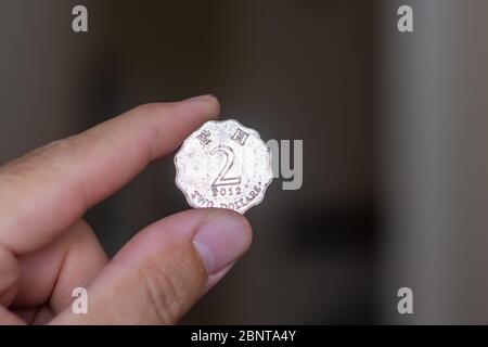 Persons hand holding out a odd shaped two dollar coin, the Currency of Hong Kong -  on a brown background. Money exchange. Stock Photo