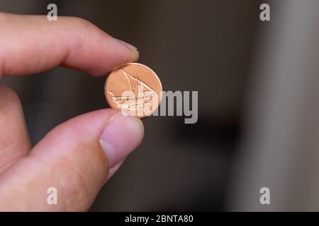 Persons hand holding out a fils coin, less than a dirham, the Currency of the United Arab Emirates -  on a brown background. Money exchange. Stock Photo