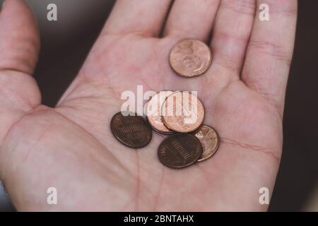 Persons hand holding out a a handful of United States of America (USA) pennies, a useless coin on a brown background. Money exchange. Stock Photo