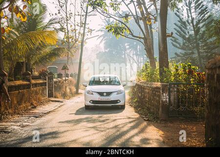 Goa, India - February 20, 2020: White Suzuki Baleno Car Moving On Country Road Through An Indian Village. Stock Photo