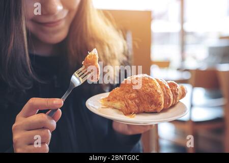Closeup image of hands cutting a piece of croissant by fork to eat on wooden table Stock Photo