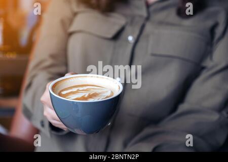 Closeup image of a woman holding and drinking hot latte coffee while sitting in cafe Stock Photo