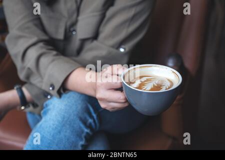 Closeup image of a woman holding and drinking hot latte coffee while sitting in cafe Stock Photo