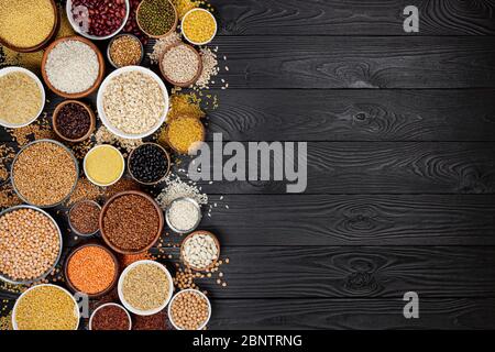 Different cereals, grains, seeds, groats, legumes and beans in bowls, top view of raw porridge collection on black wooden background with copy space Stock Photo