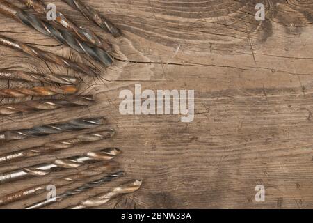 Old metal drills lie on a wooden surface. View from above. Empty space for text Stock Photo