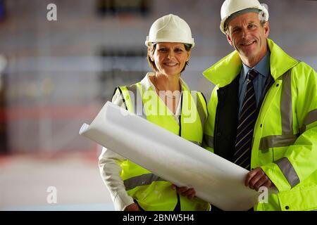 Portrait of two mature architects with blueprints standing at building site Stock Photo