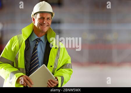 Portrait of smiling mature architect wearing a hardhat and reflective clothing holding a digital tablet on construction site Stock Photo