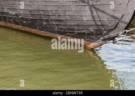 Detail of the black painted hull of an old wooden ship, green sea water copy space, horizontal aspect Stock Photo