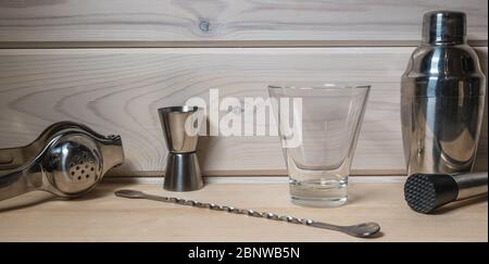 Professional bartender tools for making cocktails on wooden background. Pieces of ice and lemon near the glass of alcohol or non alcohol liquid water Stock Photo