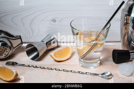 Professional bartender tools for making cocktails on wooden background. Pieces of ice and lemon near the glass of alcohol or non alcohol liquid water Stock Photo