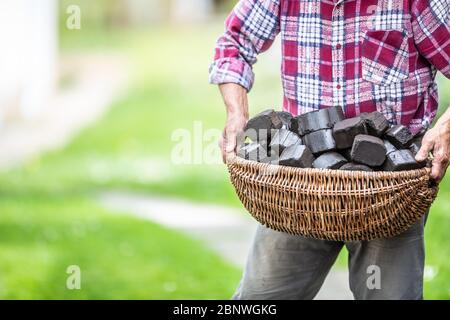 Man carrying basket full of coal briquettes in the backyard of his house. Stock Photo