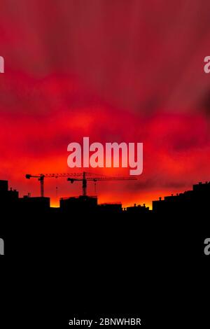 two construction cranes over standing houses against a sunset bright sky, siluet, place for text Stock Photo