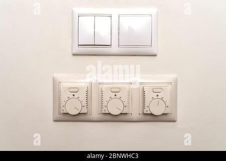 The regulator of a heat-insulated floor. On the wall there are three floor heating controls. Two light switches are installed on top. Stock Photo