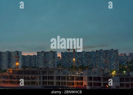 Two construction cranes over standing buildings at night. continuous infrastructure construction Stock Photo
