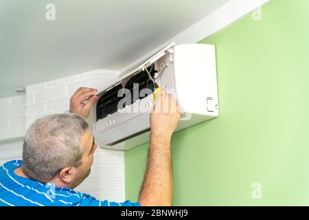 Male technician - repair and diagnostics of air conditioners. Opening the cover and removing the display for repair Stock Photo