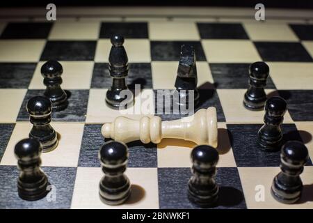 White queen fallen on the chessboard and around the black pieces Stock Photo