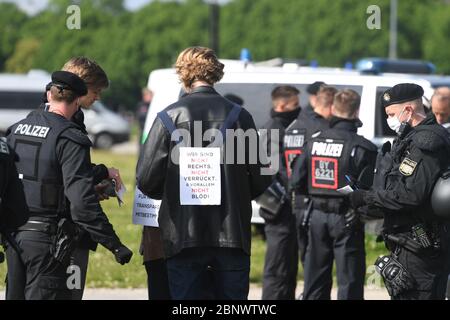 Munich, Germany. 16th May, 2020. A participant in a demonstration against the anti-Corona measures of politics stands on the Theresienwiese between policemen with a sign on his back saying 'We are not right. Not crazy and above all not stupid'. Credit: Felix Hörhager/dpa/Alamy Live News Stock Photo