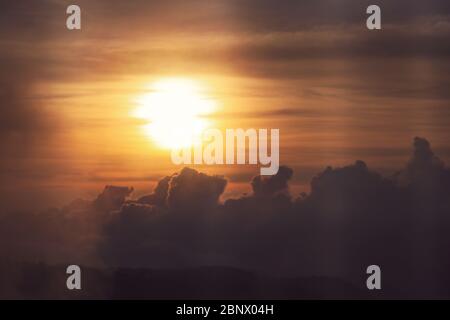 Silhouette landscape of the Sun shining gloriously through the layers of clouds during a a sunset in the mountains, clouds give a backdrop due to the Stock Photo