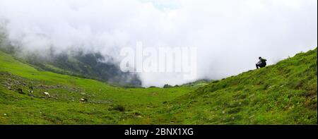 Beautiful 8K Ultra HD panorama, A person sits on the huge green meadows of Chanderkhani, where clouds float and horses graze downhill, signifying the Stock Photo