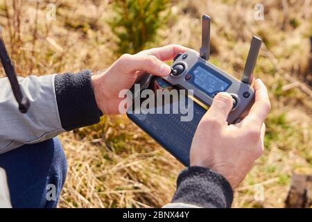 Close up mans hands holding drone remote controller with smartphone in the field. Concept of aerial shooting and flying, San Francisco, May 2020. Stock Photo