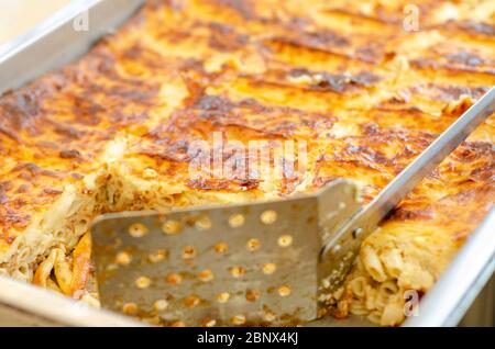 Selective focus on beveled pastitsio dish surface blurry spatula with holes, Stock Photo