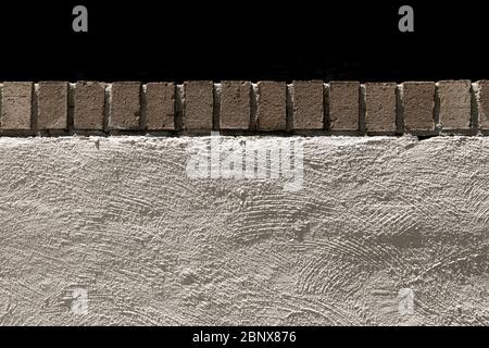 Straight on view of a trowel textured stucco retaining wall topped with row of bricks, creative copy space, horizontal aspect Stock Photo