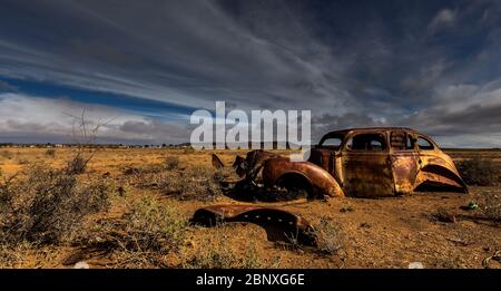 old car wreck under nice clouds in middle of nowhere Stock Photo