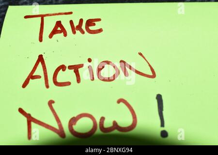 Close up of a fluorescent green color post-it note.The words "Take Action Now" are hand written on capital letters in red marker pen. Stock Photo
